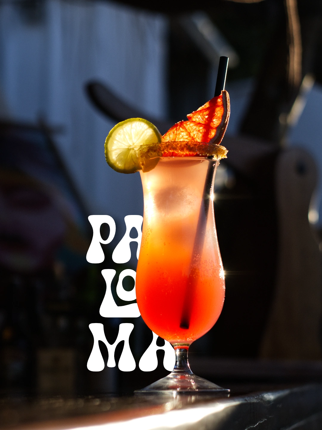 Cóctel naranja en vaso alto con lima y naranja deshidratada, junto a la tipografía original de Paloma.